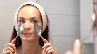 Kız aynanın önünde yemek kaşıklarıyla yüz masajı yapıyor. Yüksek kalite 4k görüntü