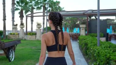 Bir kız spor kıyafetleriyle yeşil bir alanda yürüyor. Yüksek kalite 4k görüntü