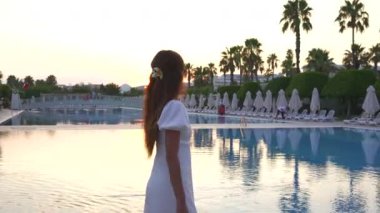 Altın saat boyunca havuzda dolaşan beyaz elbiseli bir kız. Yüksek kalite 4k görüntü