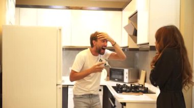 Komik bir mutfak kazasında kız, buzdolabı kapaklı adama şakayla vurur. Alnına buz koyarak cevap veriyor, onların neşeli etkileşimlerine mizahi bir dokunuş ekliyor.