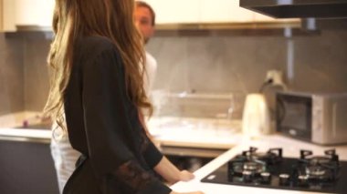 Çift mutfakta beraber çalışıyor, bulaşık makinesine koyuyor ve sohbet ederken bulaşıkları yıkıyor. Etkileşimleri sıcak ve işbirlikçi, rutin görevi keyifli ve bağlı kılıyor.