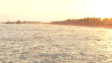 Deniz gün batımının ışınları altında parıldıyor, suyun üzerine altın bir renk döküyor. Doğanın güzelliğini ve huzurlu kıyı anlarını canlı ve sıcak tonlarda yakalamak için mükemmel. Yüksek kaliteli 4K görüntü.