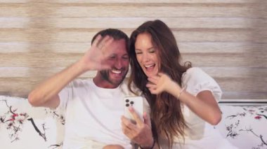 Neşeli evli bir çift kanepelerinde oturup akrabalarıyla video görüşmesi yapıyor. Gülüşlerini ve gülüşlerini paylaşıyorlar, açıkça sevdikleriyle etkileşimden ve bağlantıdan zevk alıyorlar.. 