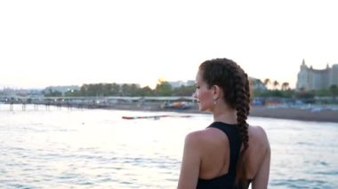Spor giyimli bir kız Akdeniz kıyısındaki iskelede geziniyor, taze okyanus esintisinin ve çarpıcı manzaranın tadını çıkarıyor. Rahatlamış tavrı, deniz kenarında mükemmel bir günün özünü yansıtıyor.