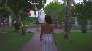 Türkiye 'nin Antalya kentinde 08.21.2024' te bir kız bir Türk otelinin manzaralı sahalarında geziniyor. Etrafı yemyeşil bahçeler ve modern mimari ile çevrili. 4k