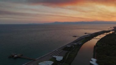 İnsansız hava aracı, deniz ile birleşen bir nehrin üzerinde çarpıcı bir gün batımı yakalar. Gökyüzünün canlı renkleri suyu yansıtıyor. Nehir ve okyanusun sakin harmanını nefes kesici bir şekilde vurguluyor.