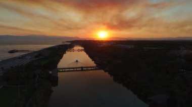Nefes kesici turuncu gün batımının altında bir nehrin denize karıştığı büyüleyici bir sahne. Çevreleyen dağlar, su yüzeyindeki yumuşak ışığı yansıtan manzarayı çerçeveler.