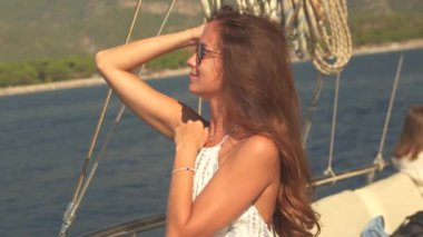 Kız yatta dinleniyor, nefes kesen doğal çevreye hayran kalıyor. Güneş gözlüklerini çıkararak, denizin ve gökyüzünün güzelliğini kucaklarken sıcak güneşin yüzünü aydınlatmasına izin veriyor.