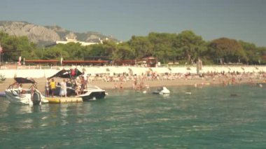 Turistler Antalya 'da kalabalık bir yaz plajında teknelere akın ediyorlar. Kıyı şeridi ziyaretçilerin sıcak güneşin, kristal berrak suların, bu popüler yerin canlı atmosferinin tadını çıkardıkları etkinliklerle dolup taşıyor.