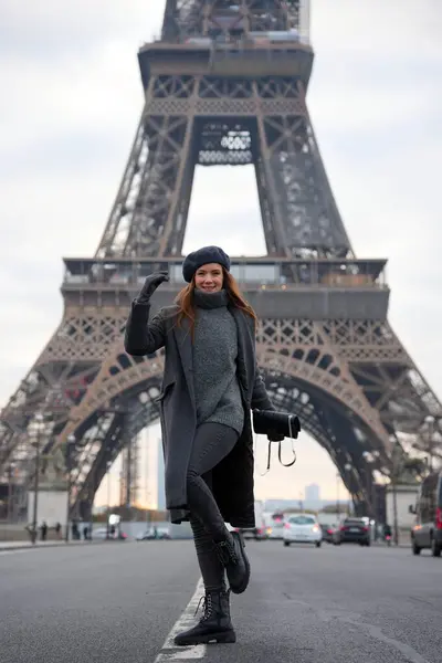Bereli ve gri paltolu Parisli kadın otoyolda güven içinde duruyor. Eyfel Kulesi de göz kamaştırıcı arka planı. Bu sahne Paris stili ve zarafetinin mükemmel bir karışımını yakalar..