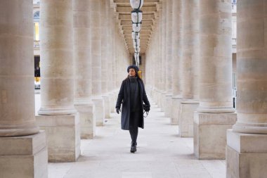 Kış kıyafetleri içinde şık bir kadın Palais Royal 'deki sütunların arasında yürür, Paris' in zarafetini ve inceliğini bu ikonik yerde yakalar..