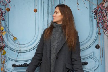 Gri kışlık ceketli bir kadın Montmartre, Paris 'te sarmaşıkla süslenmiş mavi bir kapının önünde poz veriyor. Kır manzarası ve şık elbiseler Paris 'te büyüleyici bir manzara yaratır..