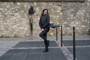 Neşeli bir kadın Montmartre, Paris 'teki tuhaf Le Passe-Muraille heykelinin yanında neşeli bir poz verir. Bu ikonik noktaya eğlenceli enerji getiriyor. Kültürel ve seyahat temaları için mükemmel..