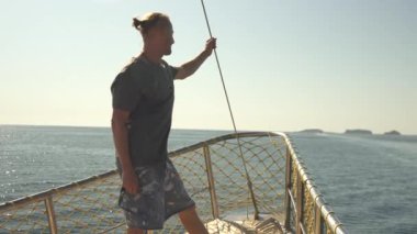 Gemilerin önünde duran genç bir adam, okyanusun ve kıyı şeridinin nefes kesici manzarasının tadını çıkarıyor. Sahne onun doğaya olan sevgisini ve denizdeki macera duygusunu yansıtıyor.