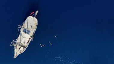 Bu büyüleyici insansız hava aracı görüntülerinde şaşırtıcı derecede canlı mavi bir denize demirlenmiş beyaz bir yat ve aşağıdaki ferahlatıcı sulara dalan turistler görülüyor. Kaliteli 4k görüntü