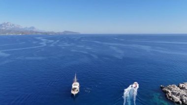 Manzaralı insansız hava aracı görüntüleri tropik bir ada kıyısı boyunca demirlemiş birden fazla yatı, turistlerin aşağıdaki kristal berrak turkuaz sularda yüzmelerinin keyfini çıkarırken yakalıyor. Kaliteli 4k görüntü