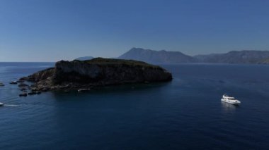 Bu güzel drone görüntüsü, temiz ve el değmemiş sularla çevrili çarpıcı bir dağ zeminine sahip bir adayı yakalıyor. Yakınlarda birkaç beyaz turist yatı var. Kaliteli 4k görüntü