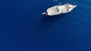 Hava görüntülerinde turistlerin güneşlendiği, yüzdüğü ve denizde huzurlu bir günün tadını çıkardığı el değmemiş turkuaz sularda demirli lüks beyaz bir yat görülüyor.. 