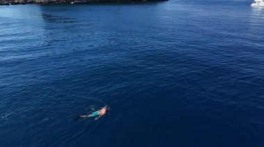 Havadan bakıldığında maske ve yüzgeçleri açık denizde süzülen yalnız bir dalgıç görülüyor. Şeffaf, turkuaz su, sualtı sularını keşfederken dalgıcın net bir görüntüsünü sağlar.