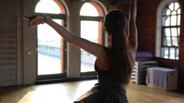 Gösterişli spor kıyafetleri içinde bir balerin, batan güneşin sıcak ışınları büyük endüstriyel pencerelerden geçerken zarif bir dans sergiliyor.