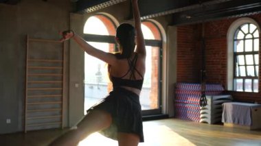 Gösterişli spor kıyafetleri içinde bir balerin, batan güneşin sıcak ışınları büyük sanayi pencerelerinden geçerken zarif bir dans sergiliyor. Yüksek kalite 4k görüntü