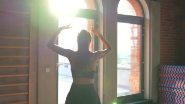 Spor giyimli balerin, batan güneşin sıcak ışınlarıyla aydınlatılan, tavan arası tarzı bir spor salonunda zarif bir dans gösterisi sergiliyor. Endüstriyel ortam, açık tuğlası ve geniş penceresiyle