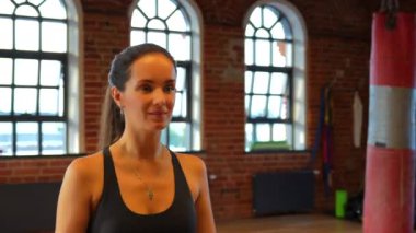 Mükemmel duruşu olan atletik bir kız modern bir spor salonundaki bir küpün üzerinde güven içinde oturur. Kamera, gücünü, dengesini ve odaklanmasını gösteren hızlandırılmış bir bakış açısı yakalıyor..