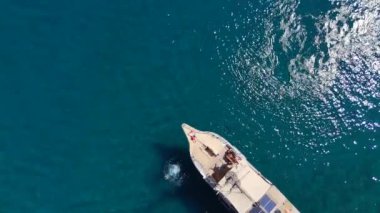Sakin bir dron çekimi, güneşin altında dinlenirken her ikisi de güneş gözlüğü takan bir yatın pruvasında uzanan genç bir çift yakalar. Uçsuz bucaksız okyanusla çevrili.