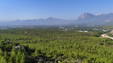 Türkiye 'nin Antalya kentindeki bir kanyon alanının nefes kesici hava manzarası, bölgenin muazzam doğal güzelliğini gözler önüne seriyor. İnsansız hava aracı yemyeşil bir ormanın üzerinde süzülüyor. Arka planda görkemli bir dağ yükseliyor..