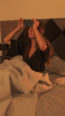 Genç bir kadın rahat yatak odasında uyumak için uzanmadan önce bir göz maskesi takarak huzurlu bir geceye hazırlanıyor. Sakin atmosfer ve yumuşak ışık sakin ve rahatlatıcı bir ortam yaratır..