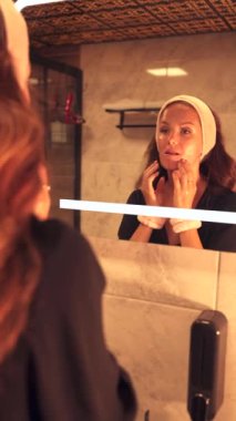 Kadın banyo aynasının önünde yüzünü nazikçe temizliyor ve günlük cilt bakımını yapıyor. Taze, temiz bir hava onun parıldayan tenini güçlendirir, sağlıklı, ışıl ışıl bir cilde teşvik eder..