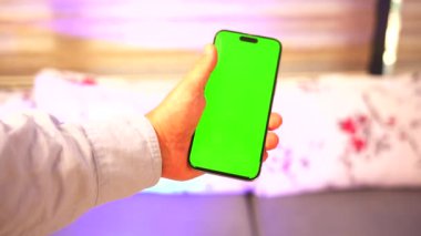 iPhone 'u yeşil ekranlı bir erkek elinde tutuyor. Uygulama promosyonu, dijital pazarlama veya kişiselleştirilebilir içerik için mükemmel. Görüntü, teknolojiyle ilgili projeler için temiz ve profesyonel bir görünüm sunuyor