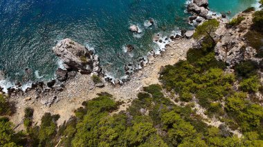 A rugged rocky shoreline with vibrant turquoise waters and lush greenery, creating a serene coastal landscape under a bright sky.  clipart