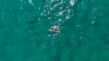 Maskeli bir dalgıç zarifçe yüzüyor ve açık denizde kristal berrak turkuaz suya dalıyor, bir dron tarafından güzelce yakalanıyor..