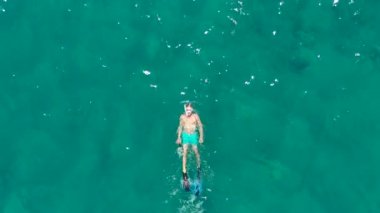 Maske takan bir dalgıç, açık denizde temiz turkuaz suyla zarifçe yüzer, İHA görüntüleriyle güzelce yakalanır, sakin okyanus ortamını gözler önüne serer.. 