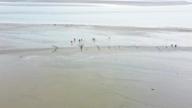 Mont Saint-Michel yakınlarındaki gelgit düzlüklerinde yürüyen ziyaretçilerin hava görüntüsü çarpıcı manzarayı ve bölgenin tarihi cazibesini yakalıyor.. 