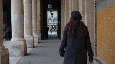 Gri bereli ve paltolu Parisli bir kadın Palais Royal 'in klasik taş sütunlarının yanında yürüyor, zamansız Fransız zarafeti sergiliyor.. 