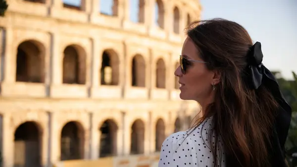 Güneş gözlüğü takan ve siyah saçlı şık bir kadın İtalya, Roma 'daki tarihi Kolezyum' a düşünceli bir şekilde bakıyor.. 