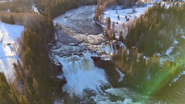 A scenic aerial view of a winding winter river in Norway, surrounded by snow-covered forests and fields. The river sparkles under soft golden sunlight. clipart