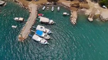 Türkiye 'nin Antalya kentinde, turkuaz sular ve kıyı cazibesiyle çevrili küçük bir limana yanaşmış teknelerin hava görüntüsü