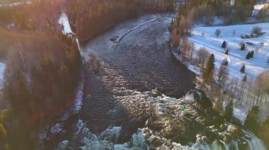 İsveç 'te karlı tarlalar, buzlu ağaçlar ve parıldayan altın güneş ışığıyla çevrili dolambaçlı bir nehrin çarpıcı görüntüsü.. 