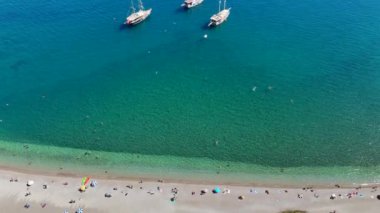 Açık denizi kaplayan bir dronun panoramik görüntüsü, canlı bir turistik plaj ve açık denizde yüzen yatlar.. 