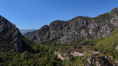 Güneşli bir günde Türkiye 'de engebeli, kayalık dağların zeminine kurulmuş kalabalık bir plajı görüntüleyen İHA görüntüsü. 