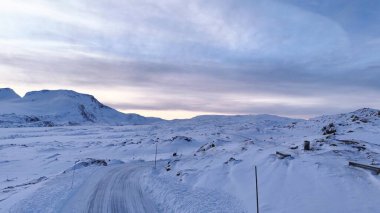 Norveç 'te nefes kesen karlı bir dağ manzarası dolambaçlı bir yol, sakin bir kış gökyüzü ve el değmemiş bir doğa içerir.. 