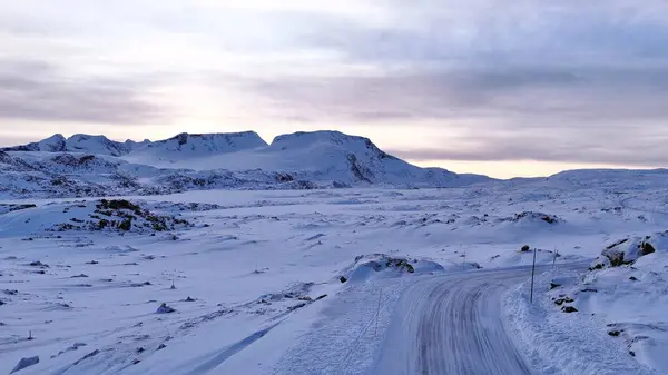 Norveç 'te nefes kesen karlı bir dağ manzarası dolambaçlı bir yol, sakin bir kış gökyüzü ve el değmemiş bir doğa içerir.. 