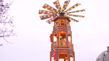 Güzel aydınlatılmış ahşap bir Noel piramidi kulesi Paris Noel pazarını süslüyor ve festival sahnesine sıcaklık ve gelenek katıyor.. 