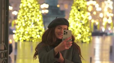 Neşeli bir kadın, Paris 'te parıldayan Noel ışıklarının önünde selfie çeker ve büyülü tatil atmosferini yakalar.. 