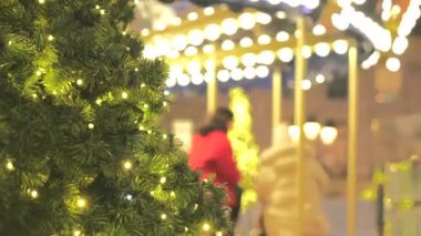 Güzel ışıklandırılmış bir Noel ağacı renkli bir atlıkarıncanın önünde duruyor ve neşeli bir tatil atmosferi yaratıyor.. 