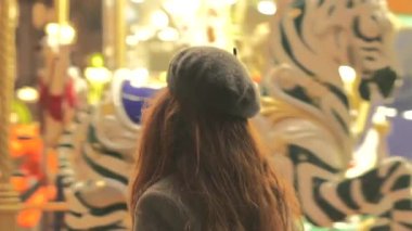 Bereli şık bir kadın, Paris 'te yağmurlu bir akşamda atlıkarıncaya binmekten zevk alır. Parlak ışıklar ve şehir cazibesiyle çevrilidir..