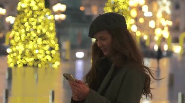 Şık bir kadın, Paris 'teki Place Vendome' da parıldayan Noel ışıklarıyla çevrili akıllı telefonunu kullanıyor. Bayram atmosferinin tadını çıkarıyor..